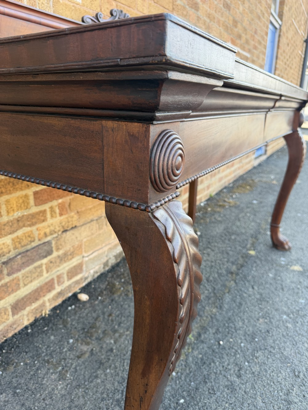 A large early 19th-century George IV mahogany serving table featuring a raised gallery back with carved cresting, carved cabriole front legs, and lion paw feet. View XIV
