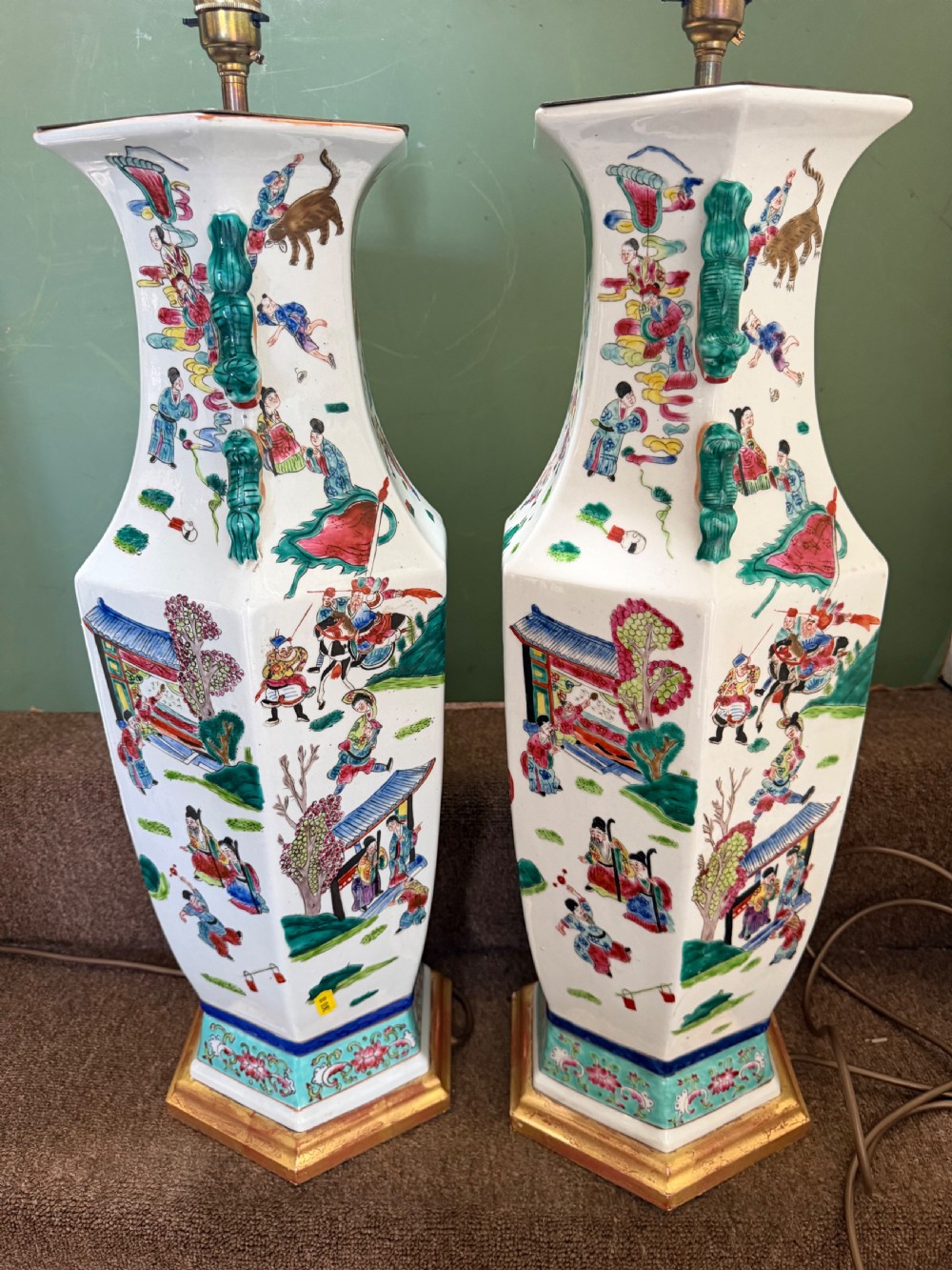 A pair of hexagonal Chinese famille-verte porcelain lamps decorated with figures in traditional scenes and set on gilded bases. View III