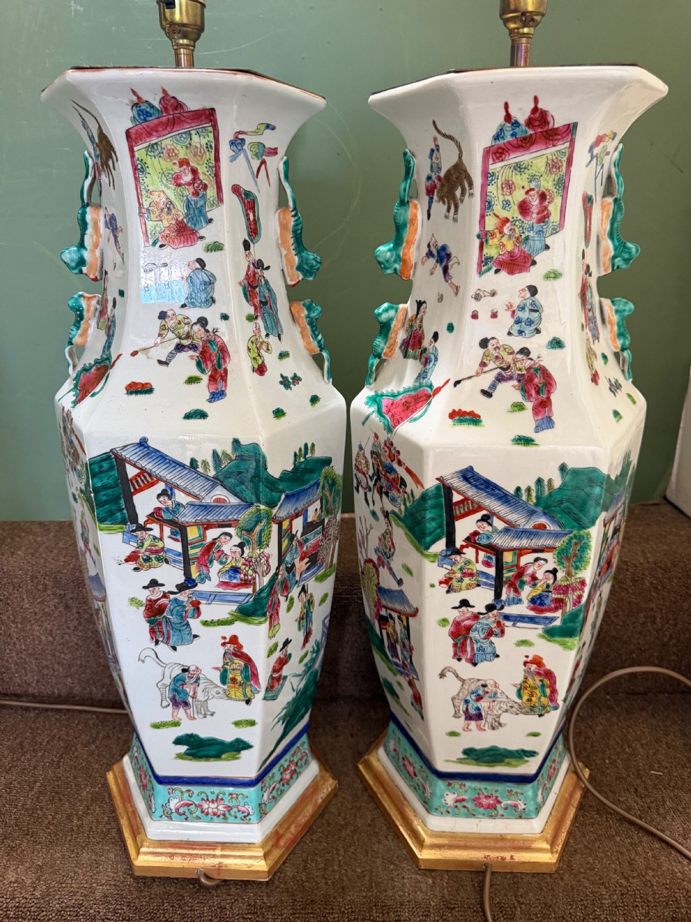 A pair of hexagonal Chinese famille-verte porcelain lamps decorated with figures in traditional scenes and set on gilded bases. View IV