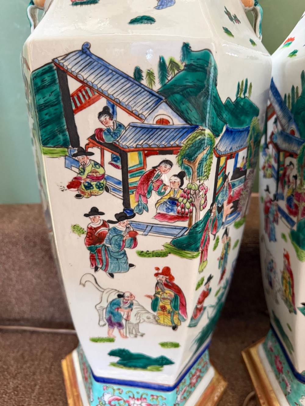 A pair of hexagonal Chinese famille-verte porcelain lamps decorated with figures in traditional scenes and set on gilded bases. View VI