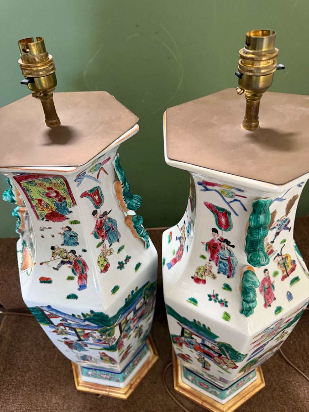 A pair of hexagonal Chinese famille-verte porcelain lamps decorated with figures in traditional scenes and set on gilded bases. View VIII