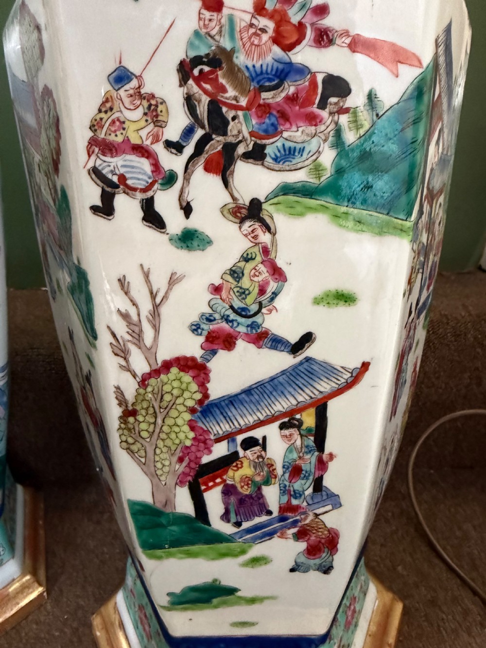 A pair of hexagonal Chinese famille-verte porcelain lamps decorated with figures in traditional scenes and set on gilded bases. View IX