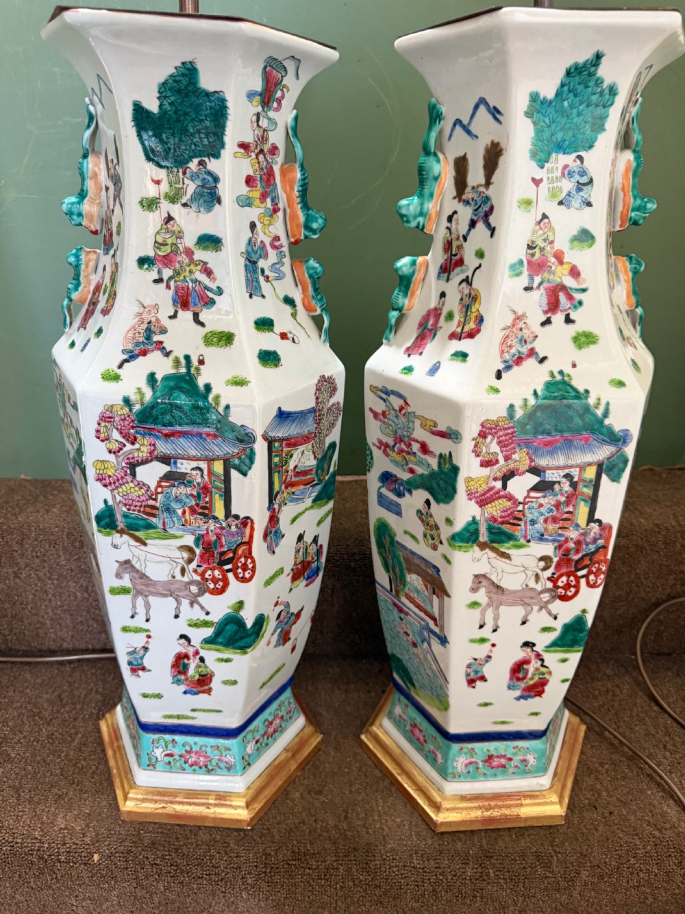A pair of hexagonal Chinese famille-verte porcelain lamps decorated with figures in traditional scenes and set on gilded bases. View X