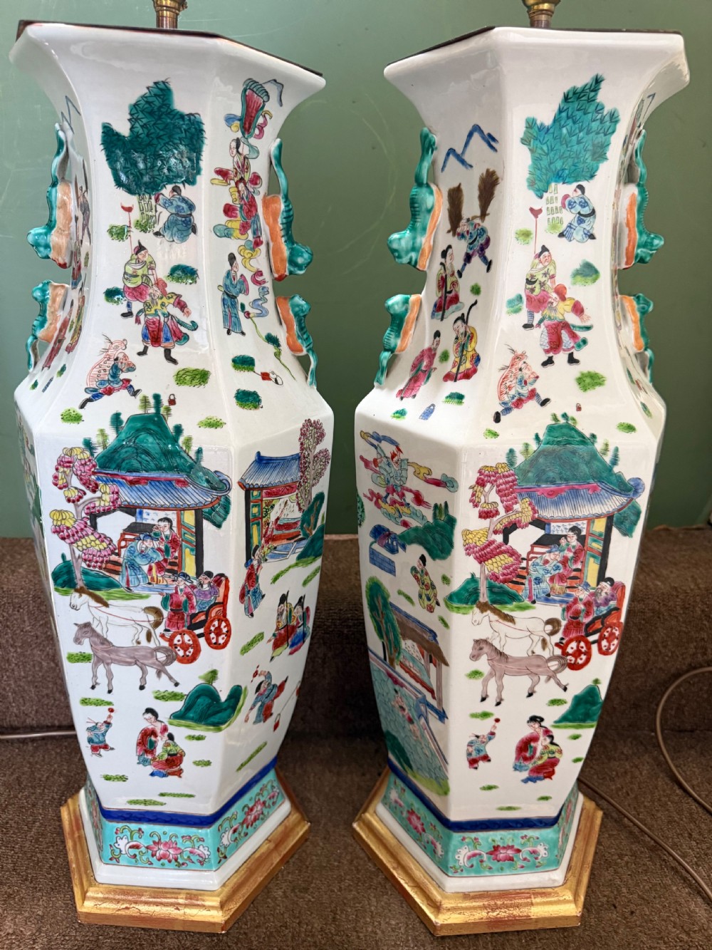 A pair of hexagonal Chinese famille-verte porcelain lamps decorated with figures in traditional scenes and set on gilded bases. View XIV