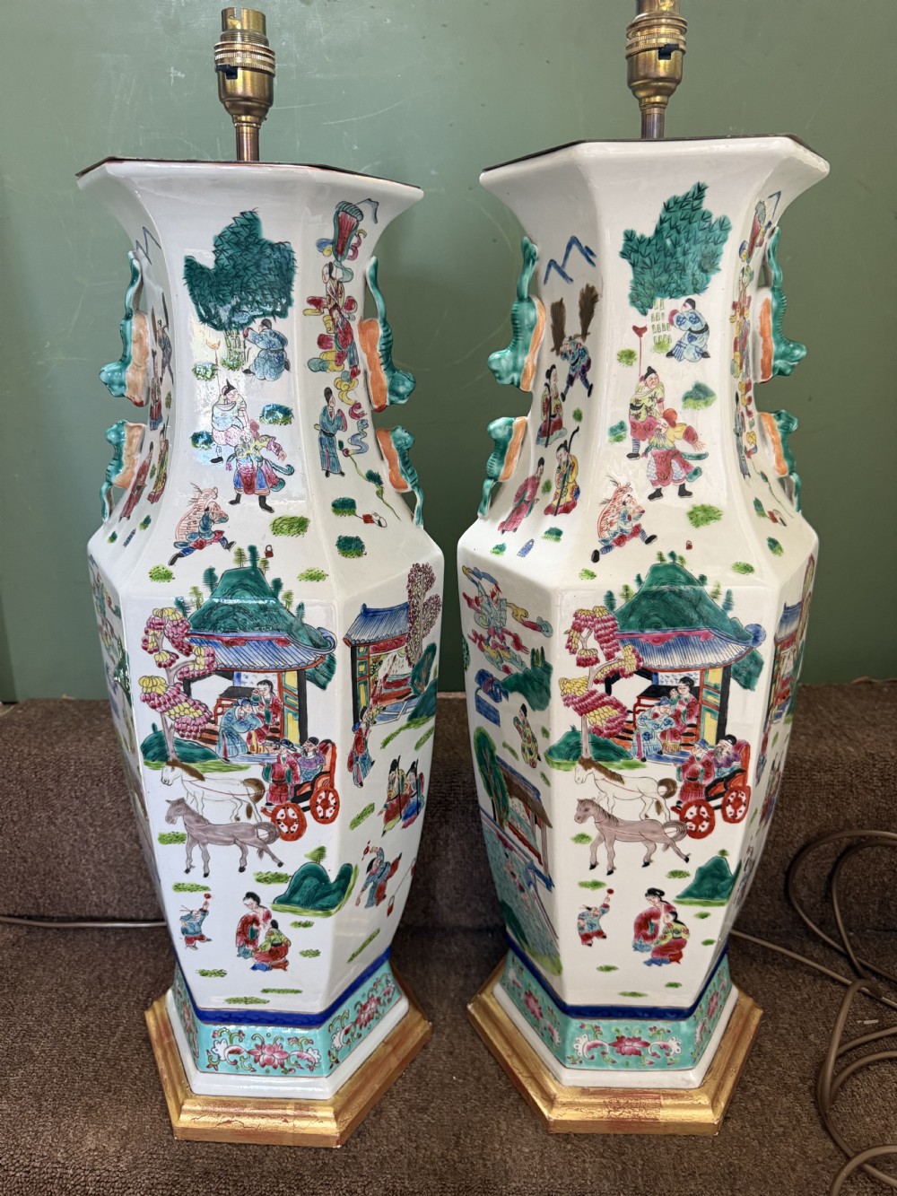 A pair of hexagonal Chinese famille-verte porcelain lamps decorated with figures in traditional scenes and set on gilded bases. View XVIII