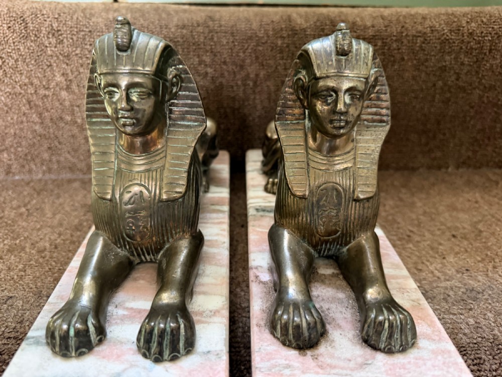 A pair of bronze recumbent sphinx sculptures featuring detailed Nemes headdresses mounted on rectangular pink marble bases. View III