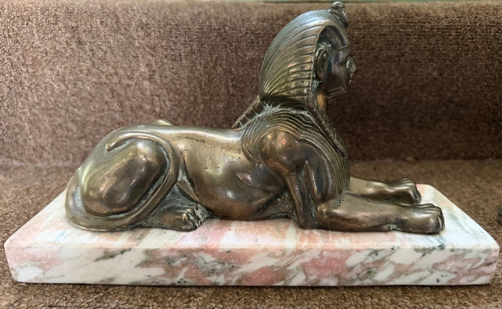 A pair of bronze recumbent sphinx sculptures featuring detailed Nemes headdresses mounted on rectangular pink marble bases. View V
