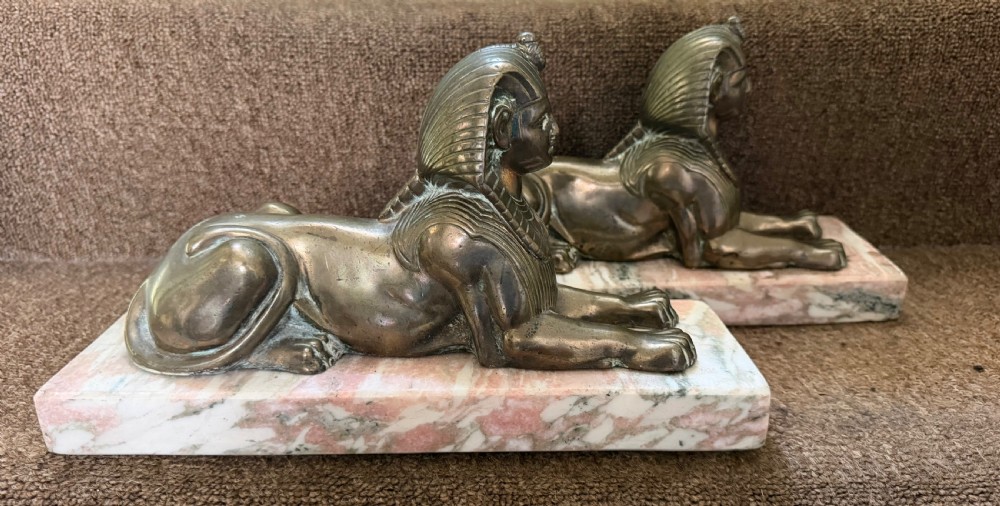 A pair of bronze recumbent sphinx sculptures featuring detailed Nemes headdresses mounted on rectangular pink marble bases. View VI