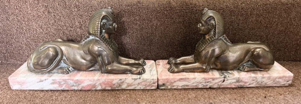A pair of bronze recumbent sphinx sculptures featuring detailed Nemes headdresses mounted on rectangular pink marble bases. View VII