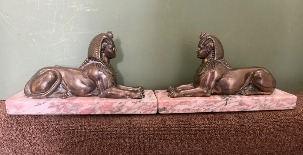 A pair of bronze recumbent sphinx sculptures featuring detailed Nemes headdresses mounted on rectangular pink marble bases. View VIII
