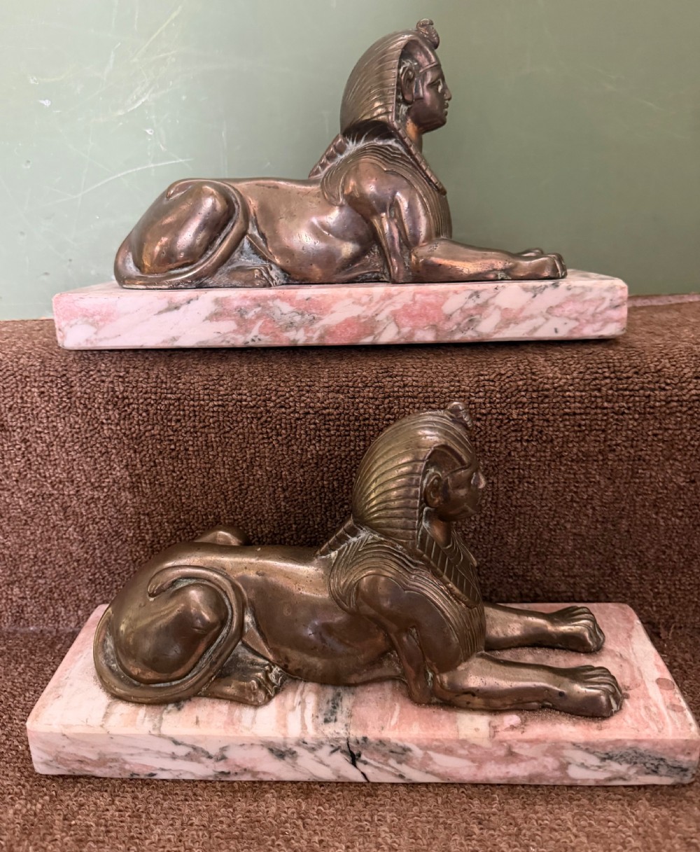 A pair of bronze recumbent sphinx sculptures featuring detailed Nemes headdresses mounted on rectangular pink marble bases. View IX