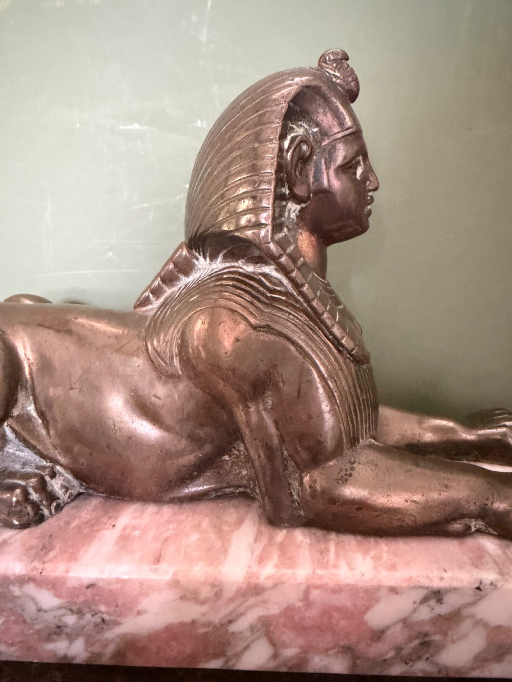 A pair of bronze recumbent sphinx sculptures featuring detailed Nemes headdresses mounted on rectangular pink marble bases. View X