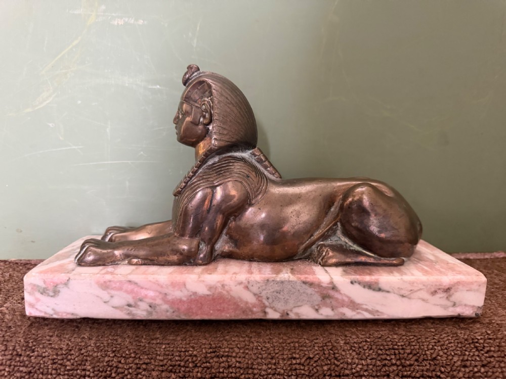 A pair of bronze recumbent sphinx sculptures featuring detailed Nemes headdresses mounted on rectangular pink marble bases. View XII