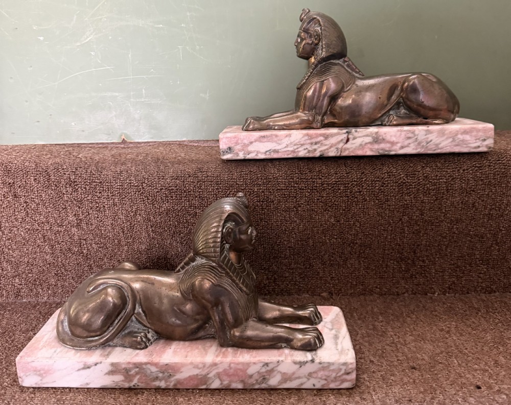 A pair of bronze recumbent sphinx sculptures featuring detailed Nemes headdresses mounted on rectangular pink marble bases. View XVI