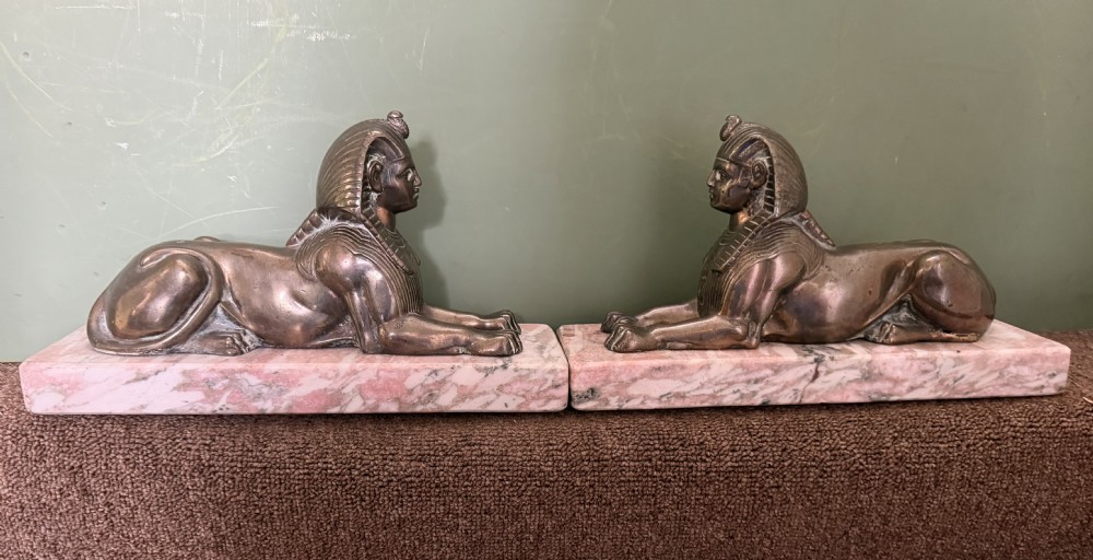 A pair of bronze recumbent sphinx sculptures featuring detailed Nemes headdresses mounted on rectangular pink marble bases. View XVIII