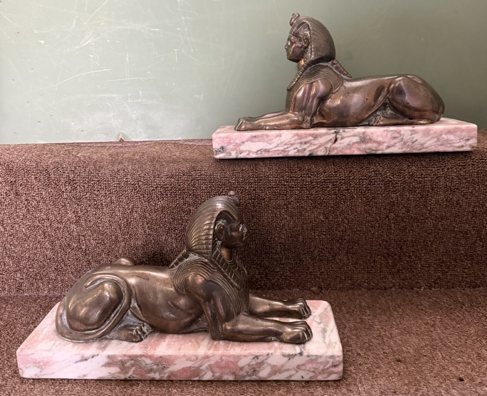 A pair of bronze recumbent sphinx sculptures featuring detailed Nemes headdresses mounted on rectangular pink marble bases. View XIX