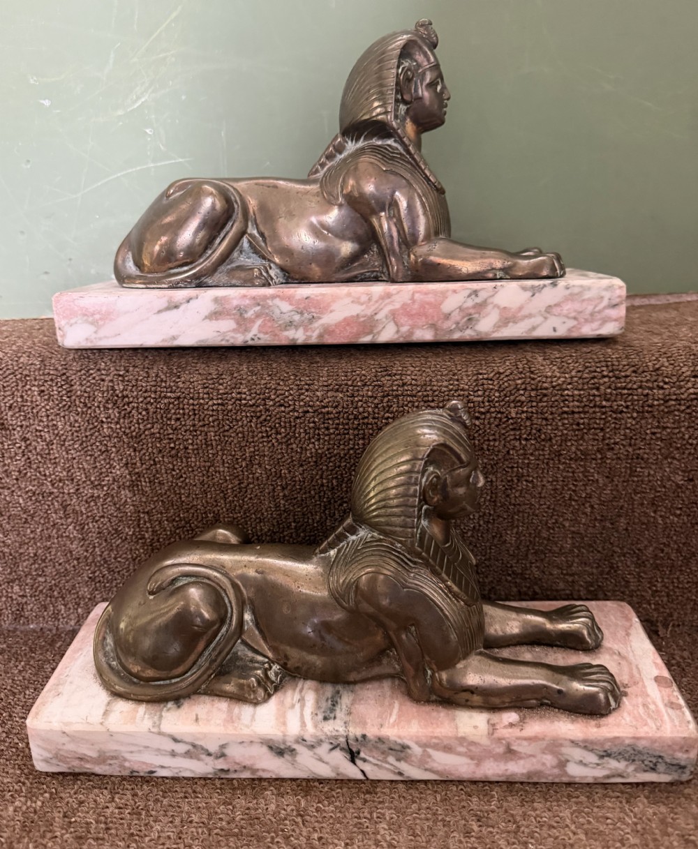 A pair of bronze recumbent sphinx sculptures featuring detailed Nemes headdresses mounted on rectangular pink marble bases. View XIV