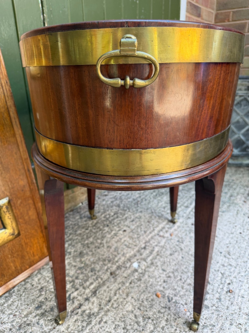 An 18th-century George III mahogany oval wine cooler with thick brass bands and brass handles, resting on a four-legged tapered stand with castors. View IV
