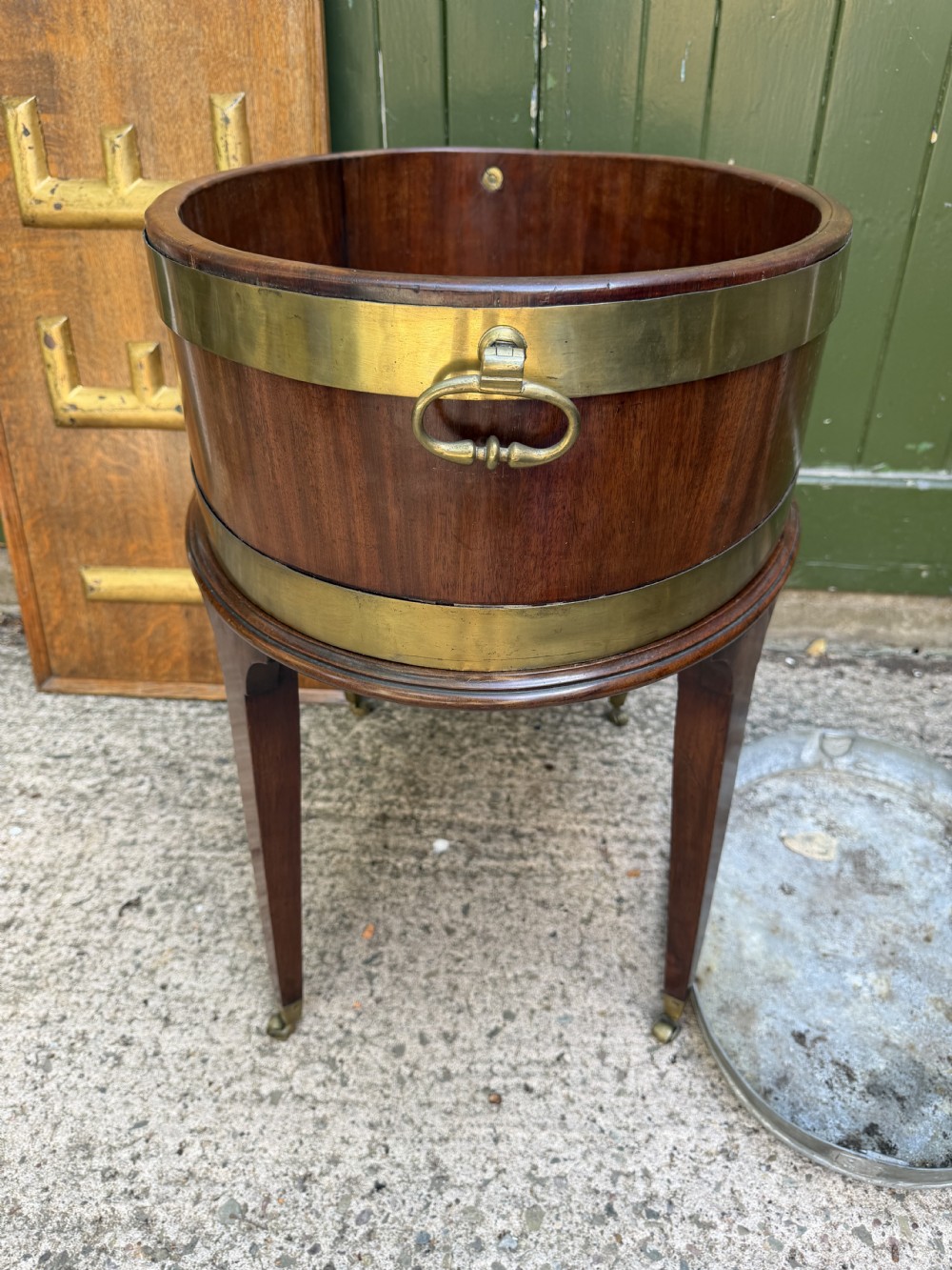 An 18th-century George III mahogany oval wine cooler with thick brass bands and brass handles, resting on a four-legged tapered stand with castors. View IX