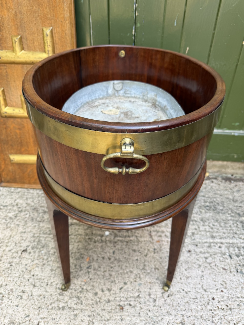 An 18th-century George III mahogany oval wine cooler with thick brass bands and brass handles, resting on a four-legged tapered stand with castors. View XI