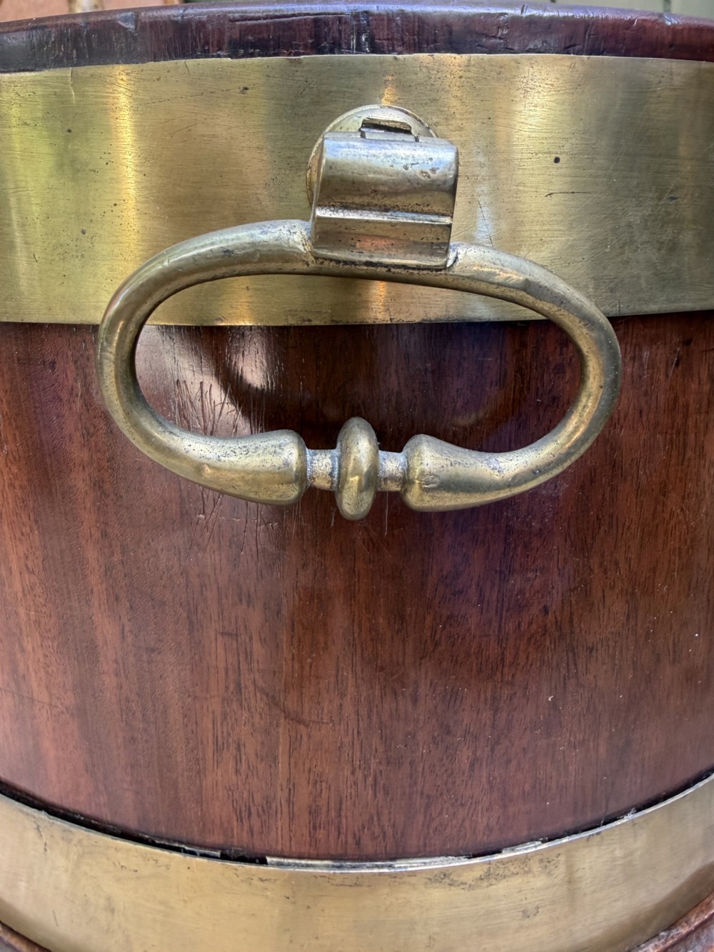 An 18th-century George III mahogany oval wine cooler with thick brass bands and brass handles, resting on a four-legged tapered stand with castors. View XII