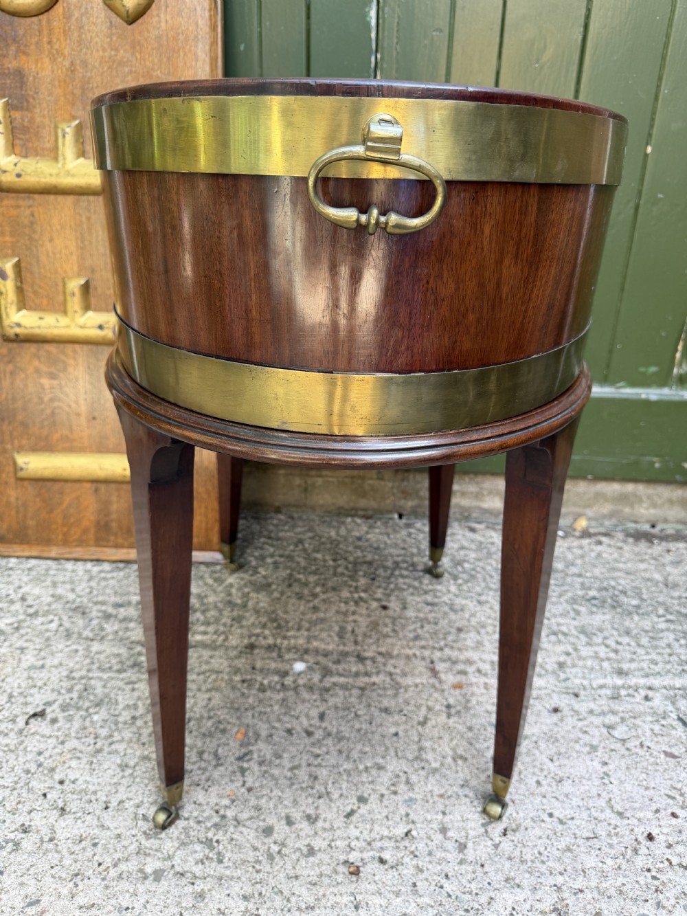 An 18th-century George III mahogany oval wine cooler with thick brass bands and brass handles, resting on a four-legged tapered stand with castors. View XIV