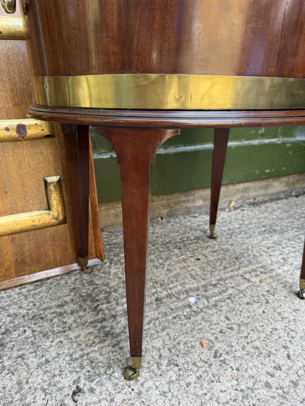 An 18th-century George III mahogany oval wine cooler with thick brass bands and brass handles, resting on a four-legged tapered stand with castors. View XVII