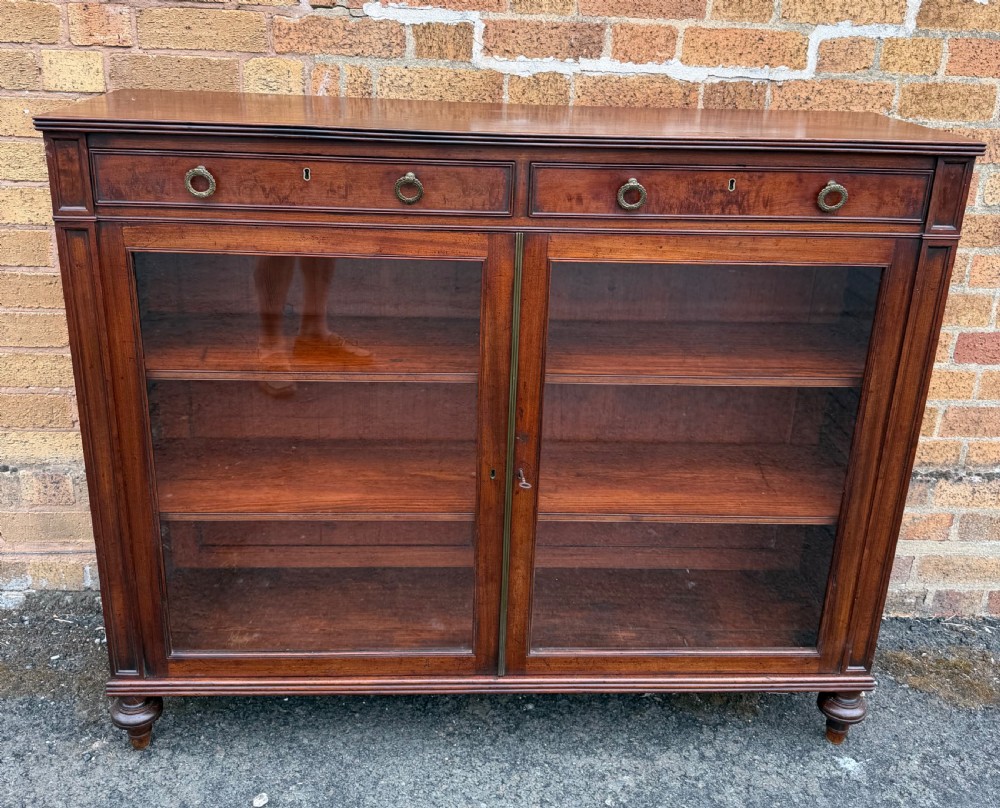 An early nineteenth-century George III mahogany low bookcase featuring two top frieze drawers over glazed twin doors and turned feet. View II