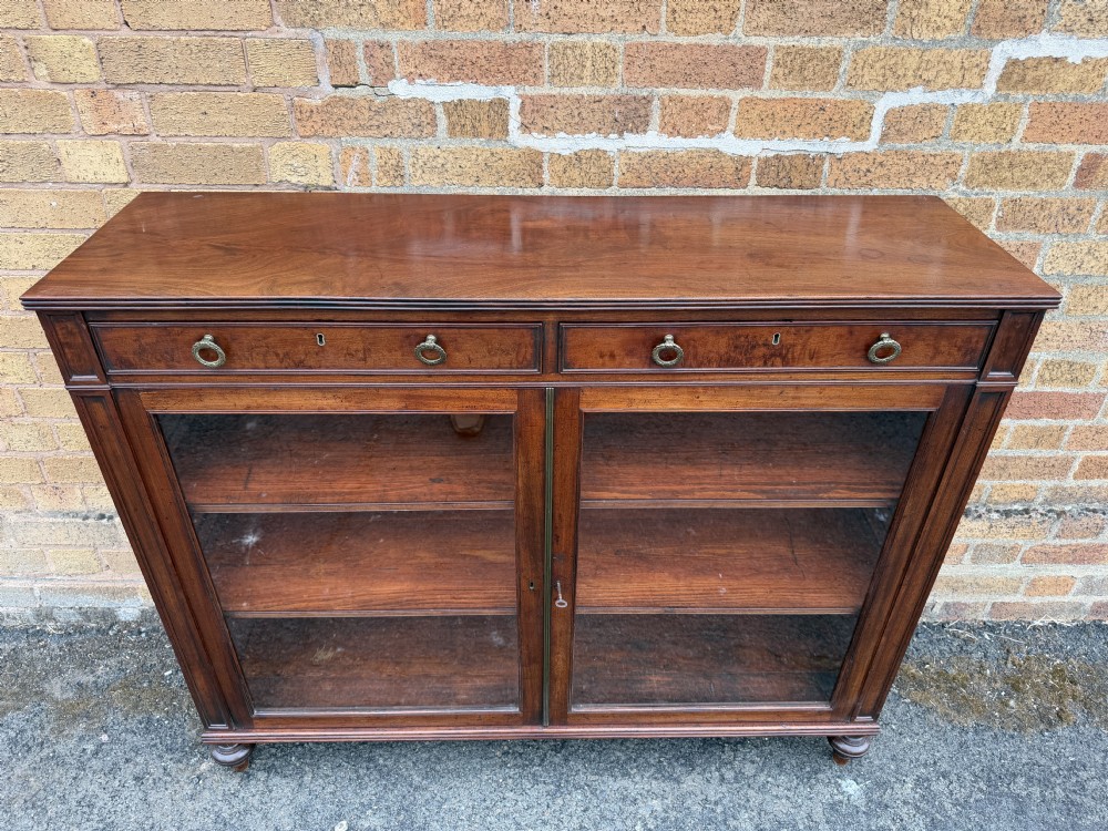 An early nineteenth-century George III mahogany low bookcase featuring two top frieze drawers over glazed twin doors and turned feet. View VI