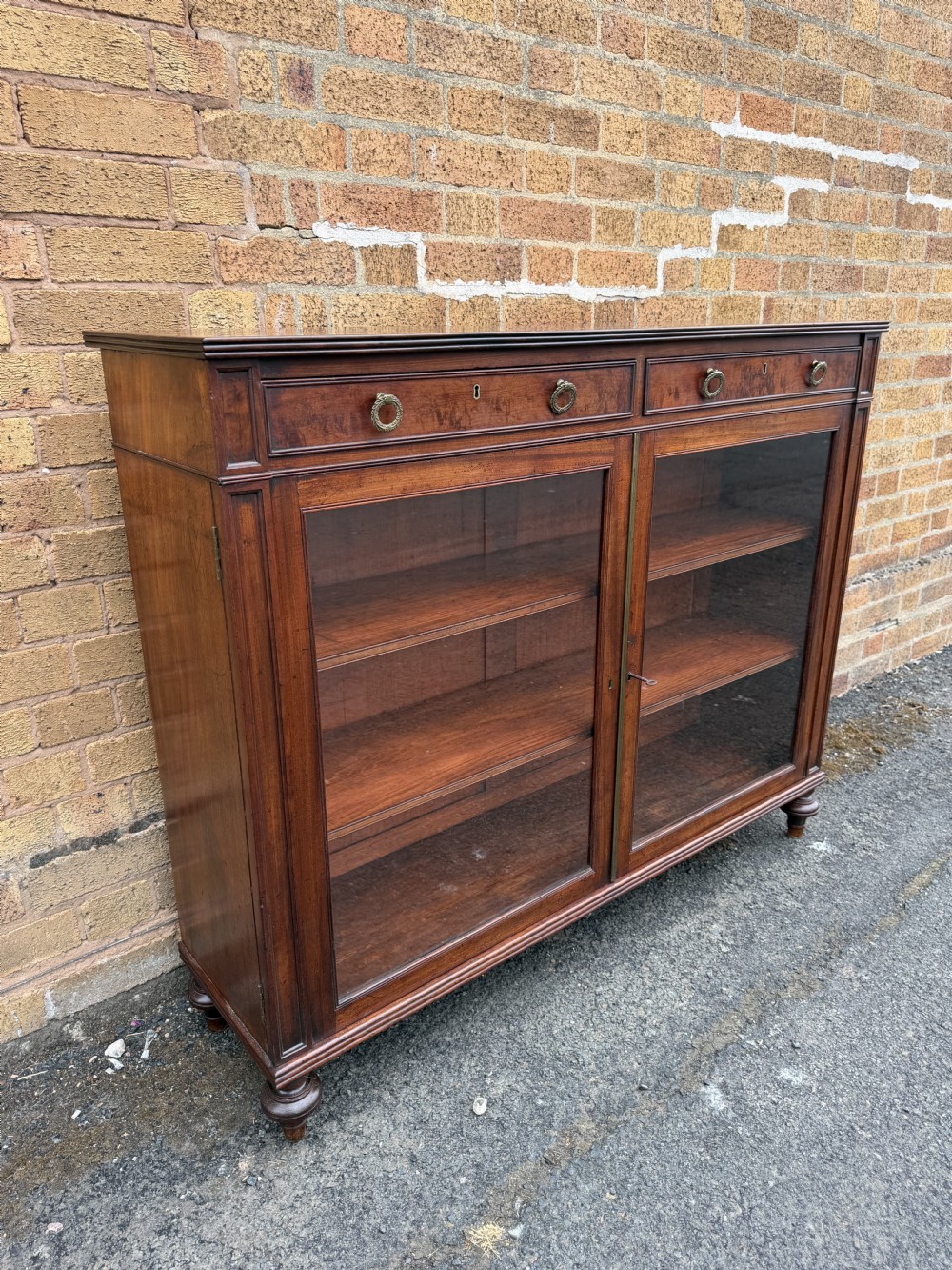 An early nineteenth-century George III mahogany low bookcase featuring two top frieze drawers over glazed twin doors and turned feet. View XVI