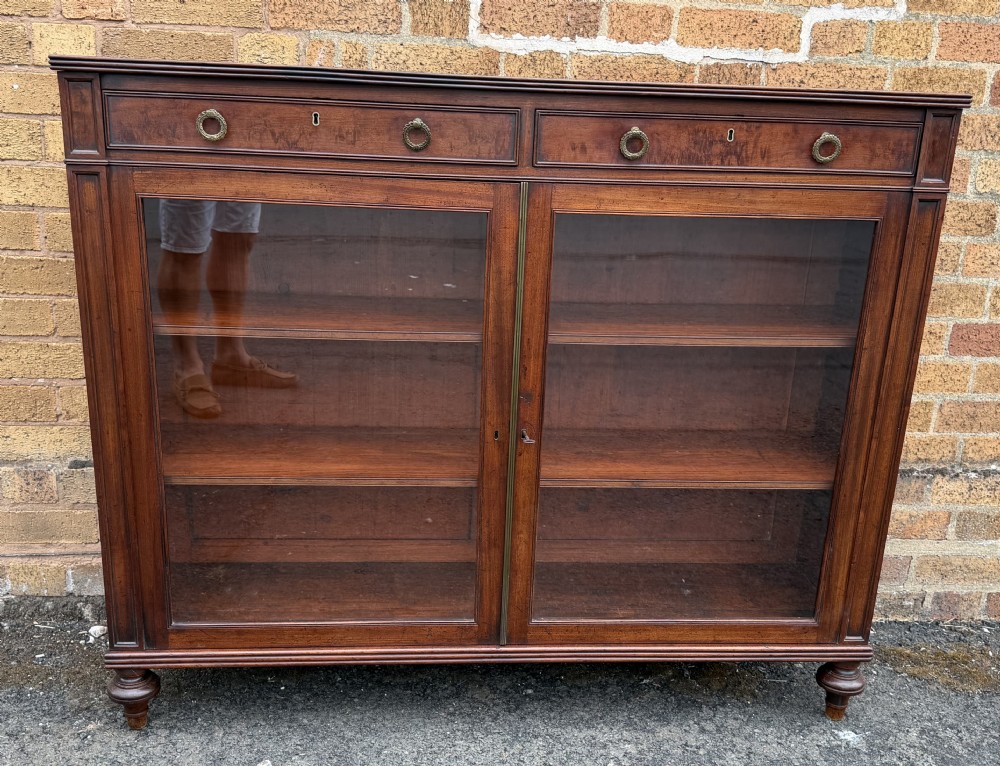 An early nineteenth-century George III mahogany low bookcase featuring two top frieze drawers over glazed twin doors and turned feet. View XXI