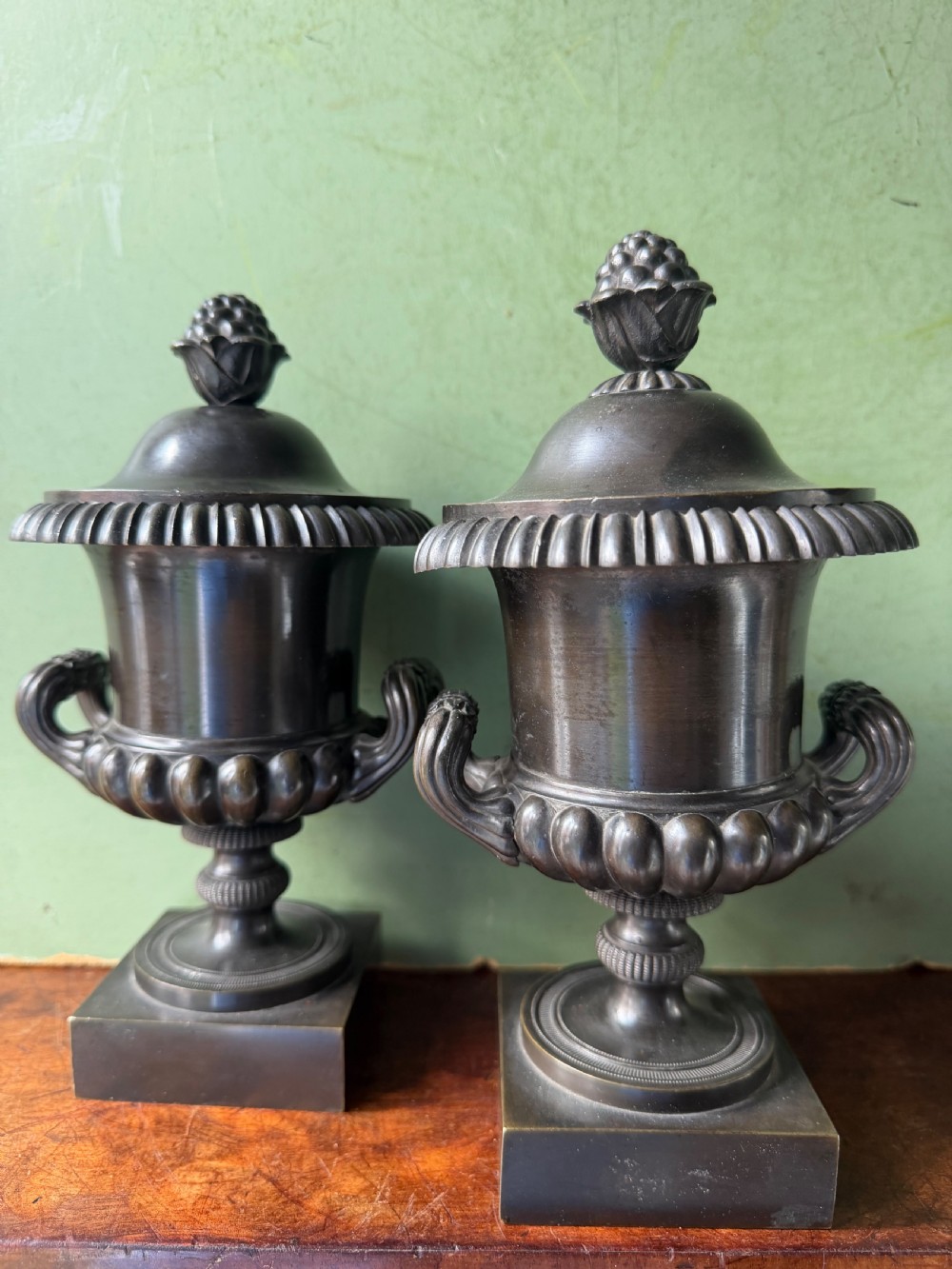 A pair of Regency patinated bronze campana-shaped cassolettes with gadrooned bodies, twin handles, pinecone finials, and square bases. View IX