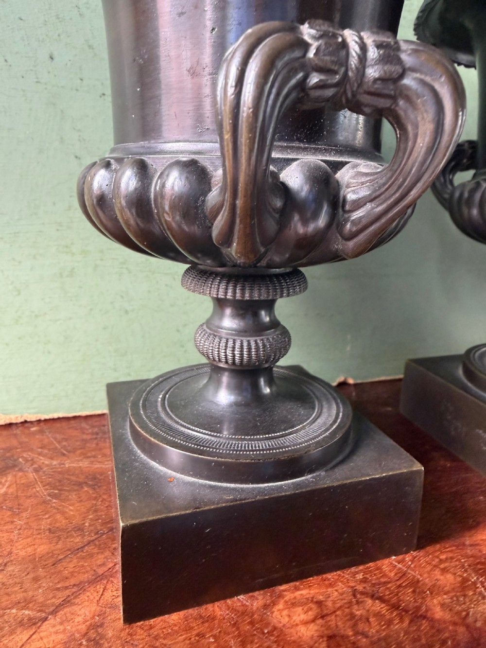A pair of Regency patinated bronze campana-shaped cassolettes with gadrooned bodies, twin handles, pinecone finials, and square bases. View X