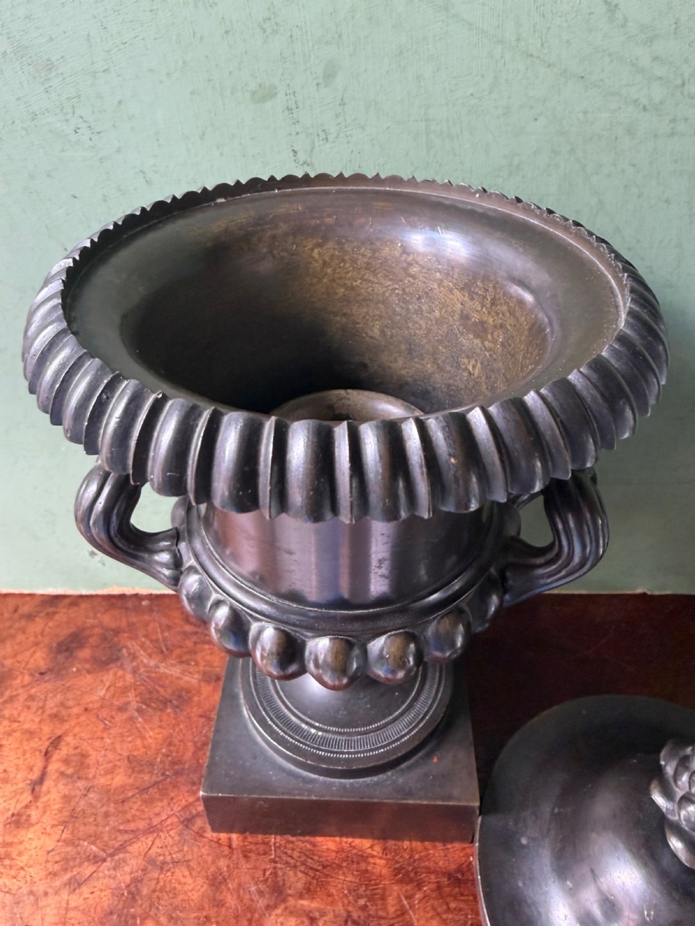A pair of Regency patinated bronze campana-shaped cassolettes with gadrooned bodies, twin handles, pinecone finials, and square bases. View XVII