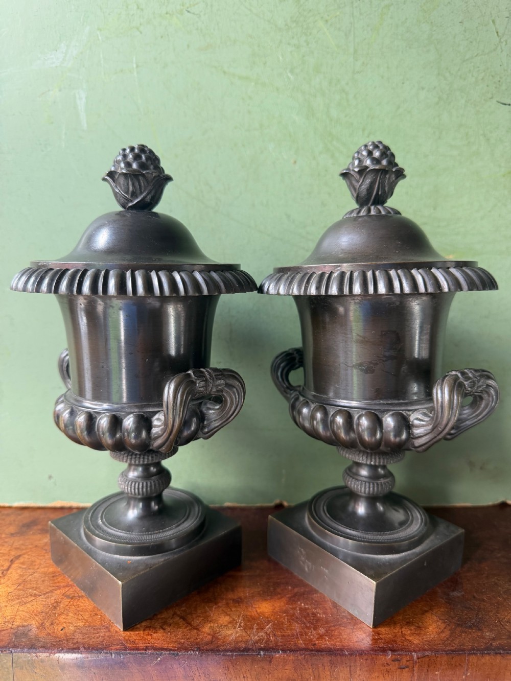 A pair of Regency patinated bronze campana-shaped cassolettes with gadrooned bodies, twin handles, pinecone finials, and square bases. View XIX