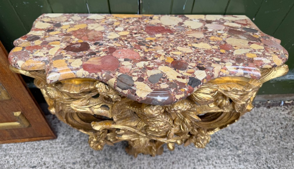 An 18th-century style French carved giltwood wall console table featuring intricate foliage, a central bird motif, and a variegated pink and ochre Breche dAlep marble top. View II
