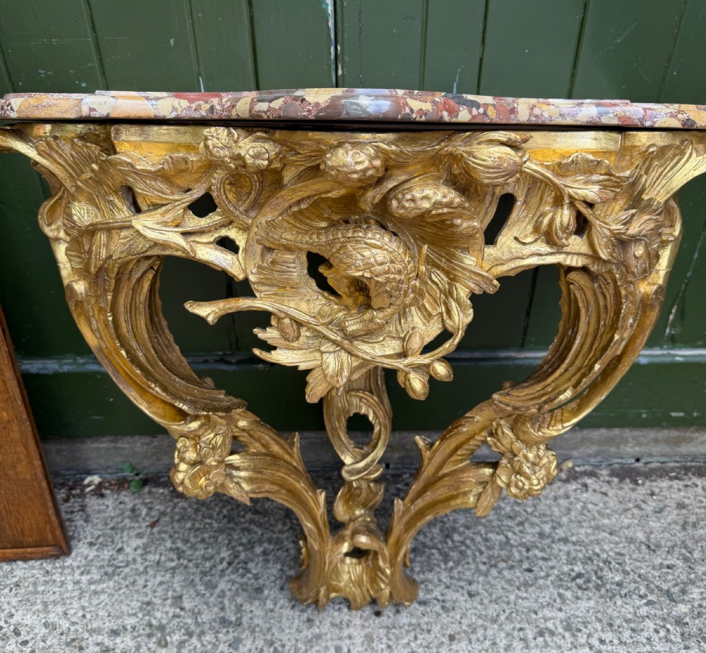 An 18th-century style French carved giltwood wall console table featuring intricate foliage, a central bird motif, and a variegated pink and ochre Breche dAlep marble top. View VII