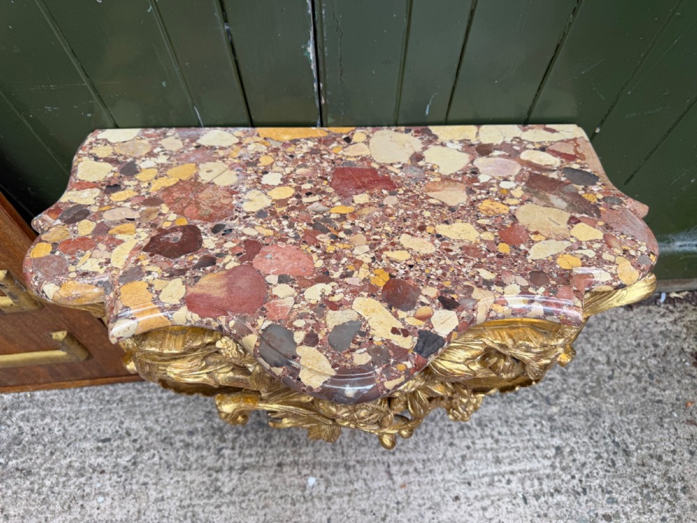 An 18th-century style French carved giltwood wall console table featuring intricate foliage, a central bird motif, and a variegated pink and ochre Breche dAlep marble top. View VIII