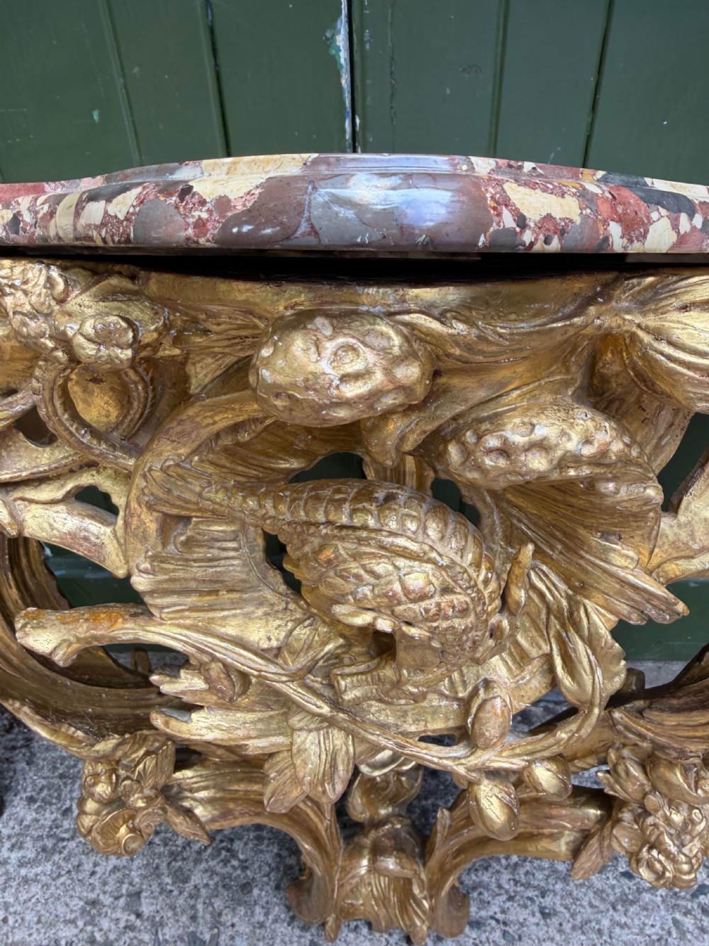 An 18th-century style French carved giltwood wall console table featuring intricate foliage, a central bird motif, and a variegated pink and ochre Breche dAlep marble top. View X