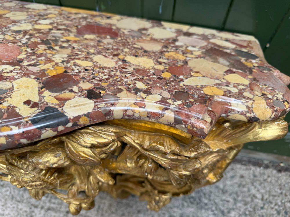 An 18th-century style French carved giltwood wall console table featuring intricate foliage, a central bird motif, and a variegated pink and ochre Breche dAlep marble top. View XII