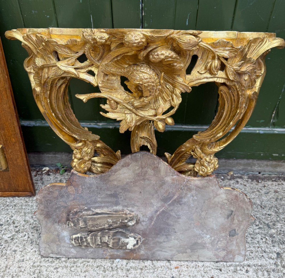 An 18th-century style French carved giltwood wall console table featuring intricate foliage, a central bird motif, and a variegated pink and ochre Breche dAlep marble top. View XIV