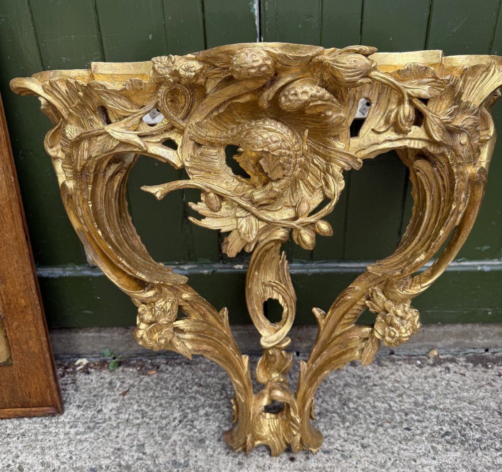 An 18th-century style French carved giltwood wall console table featuring intricate foliage, a central bird motif, and a variegated pink and ochre Breche dAlep marble top. View XV