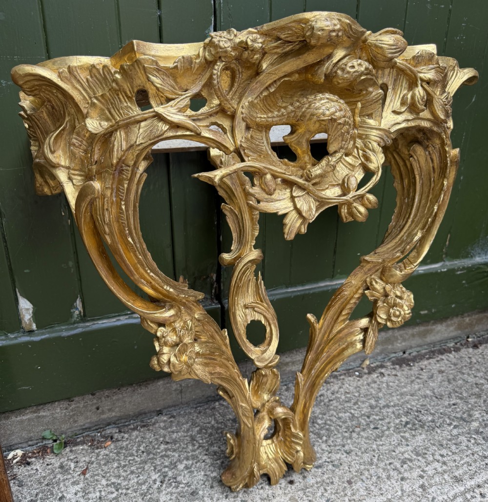 An 18th-century style French carved giltwood wall console table featuring intricate foliage, a central bird motif, and a variegated pink and ochre Breche dAlep marble top. View XVII