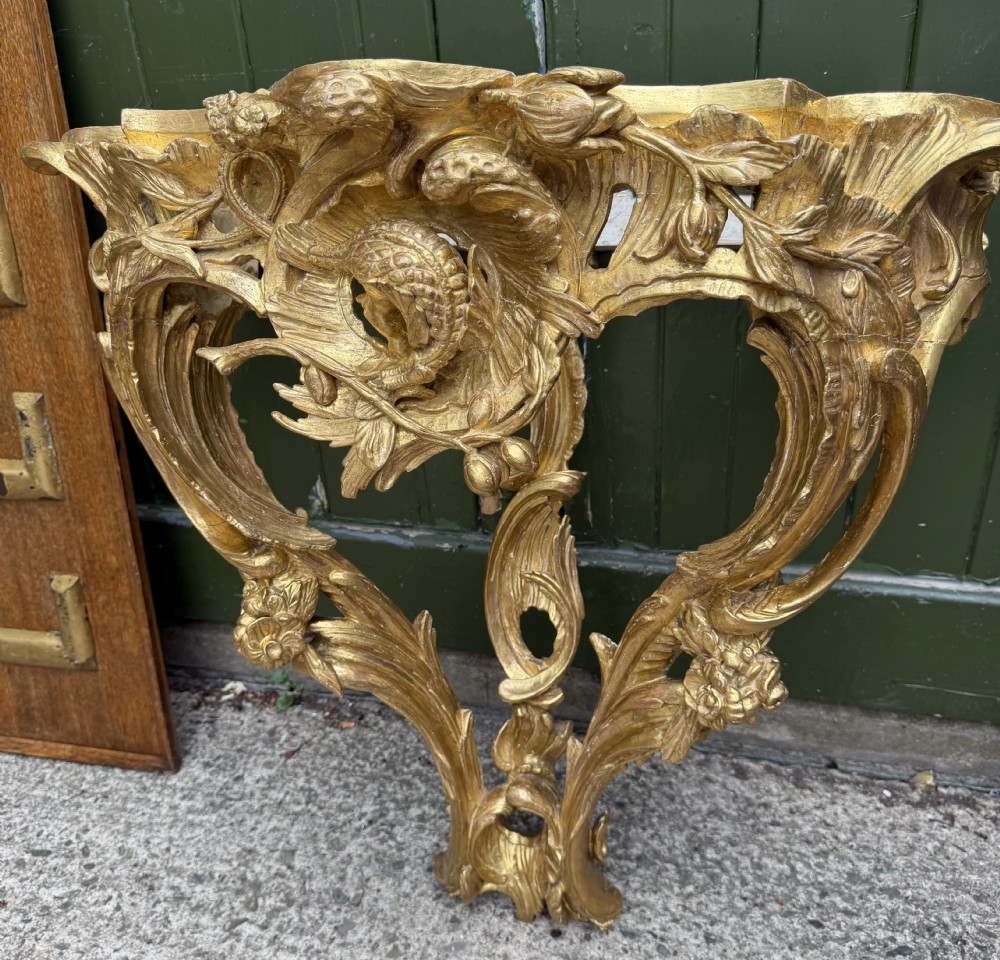 An 18th-century style French carved giltwood wall console table featuring intricate foliage, a central bird motif, and a variegated pink and ochre Breche dAlep marble top. View XVIII