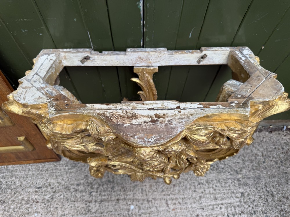 An 18th-century style French carved giltwood wall console table featuring intricate foliage, a central bird motif, and a variegated pink and ochre Breche dAlep marble top. View XIX