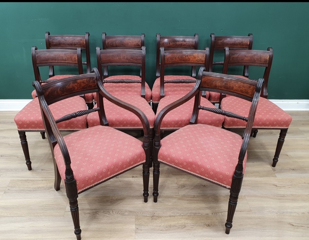 A set of ten early nineteenth-century mahogany dining chairs featuring tablet top rails, reeded front legs, and patterned pink upholstered seats.