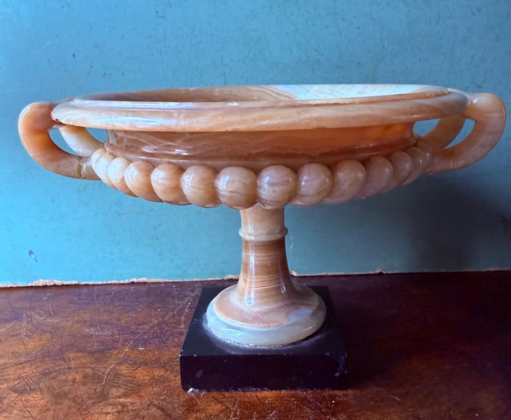 A pair of 19th-century carved amber alabaster tazze with gadrooned rims and twin loop handles set on square black marble plinths. View VI