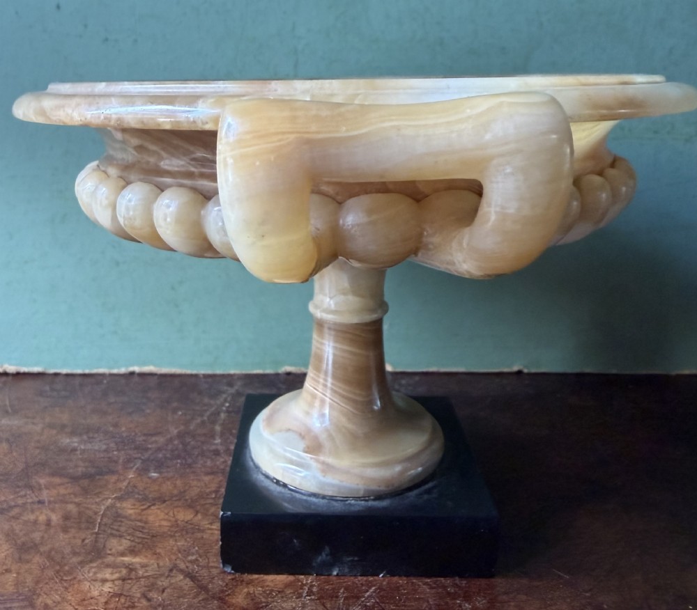 A pair of 19th-century carved amber alabaster tazze with gadrooned rims and twin loop handles set on square black marble plinths. View XII