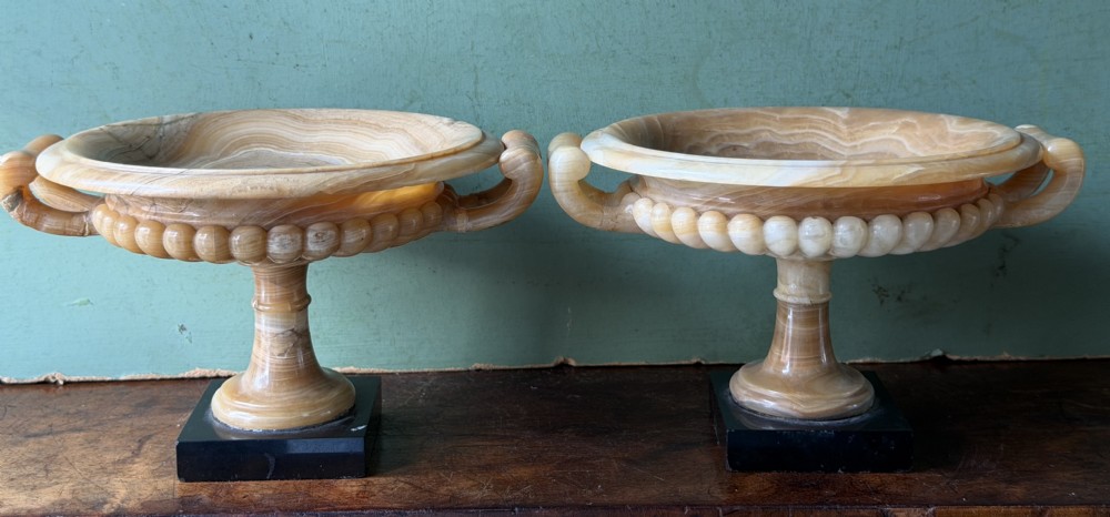 A pair of 19th-century carved amber alabaster tazze with gadrooned rims and twin loop handles set on square black marble plinths. View XV