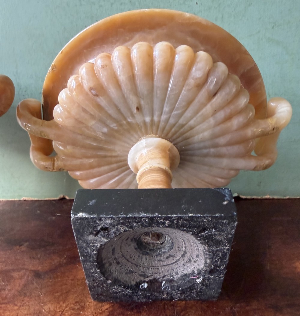 A pair of 19th-century carved amber alabaster tazze with gadrooned rims and twin loop handles set on square black marble plinths. View XIX
